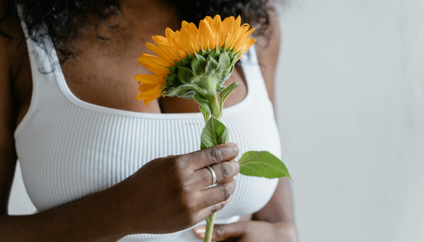 Close-up of woman in white top holding a bright sunflower, focusing on hands and flower.