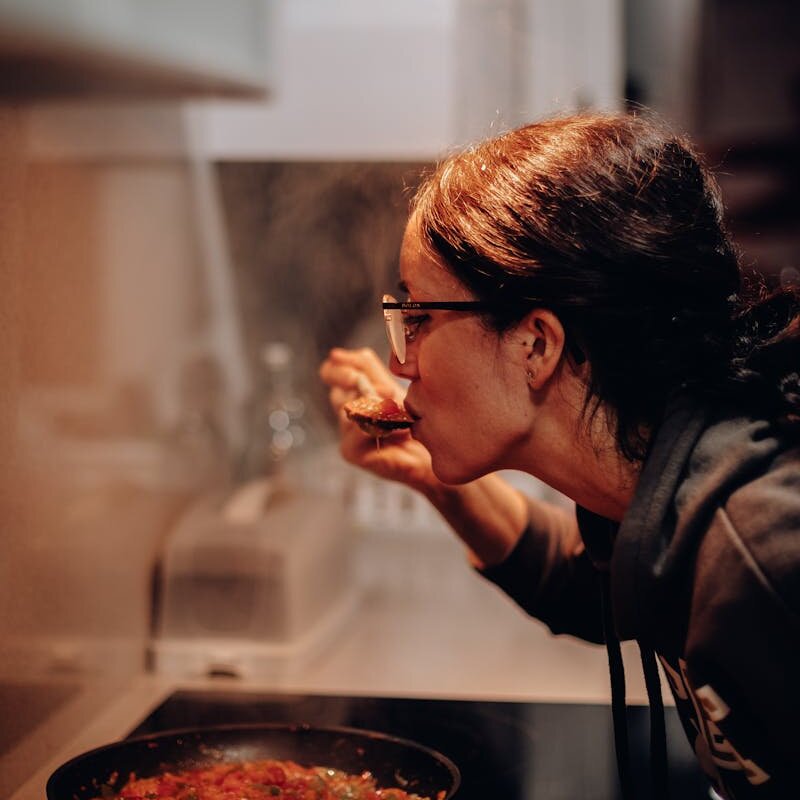 Woman cooking and tasting a dish on the stove, showcasing home culinary expertise.