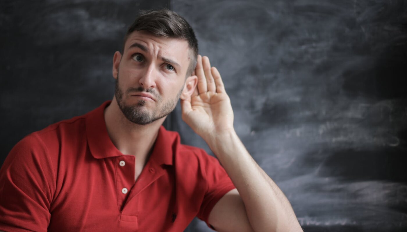 Thoughtful man listening intently against a chalkboard background in a red polo shirt.