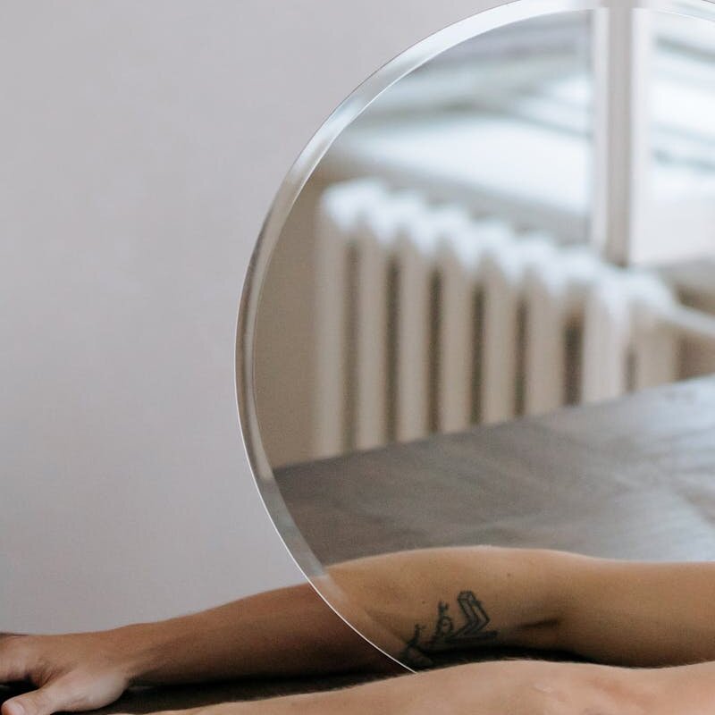 Artistic capture of arms with tattoo reflected in a circular mirror indoors.